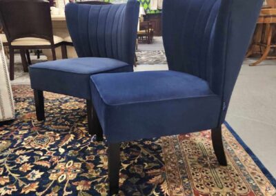 Pair of elegant blue upholstered chairs with wooden legs on a patterned rug.