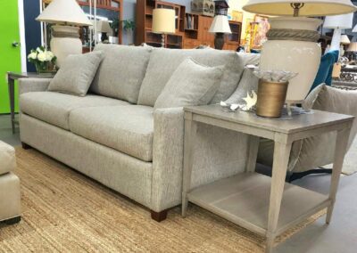 Modern gray sofa with matching side table, lamp, and decorative items in a showroom.