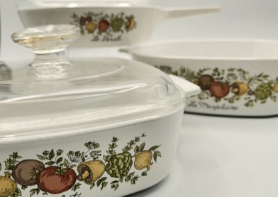 Vintage white casserole dishes with floral and fruit patterns and glass lids.