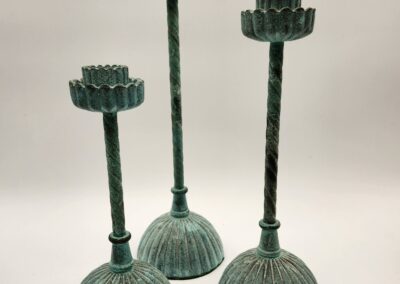 Three greenish metal candle holders of varying heights with round bases.