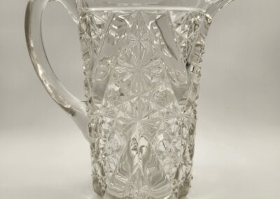 Clear glass pitcher with intricate cut patterns and a handle.