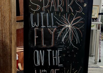 Chalkboard sign with fireworks drawing and text about sparks flying on the 4th.