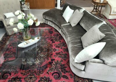 Elegant curved gray sofa with cushions around a glass coffee table on a red patterned rug.