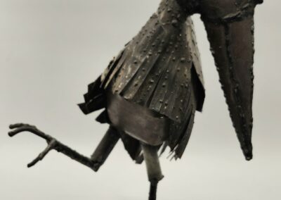Metal bird sculpture balancing on one leg with a playful pose.
