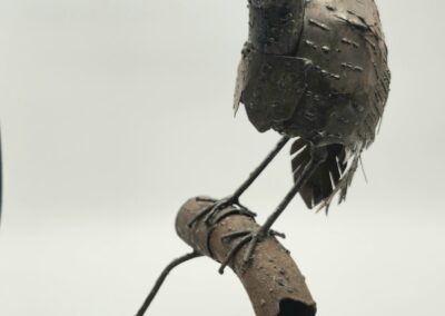 Metal bird sculpture perched on a cork branch.