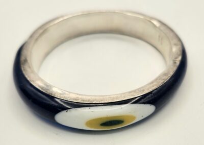 A silver ring with a black and white design featuring a green and yellow eye motif.
