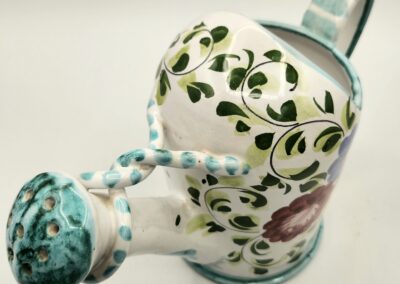 Decorative ceramic watering can with floral designs and a turquoise spout.