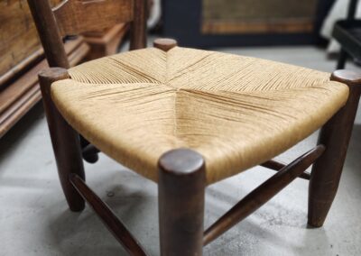 Rustic wooden stool with woven seat in a vintage setting.