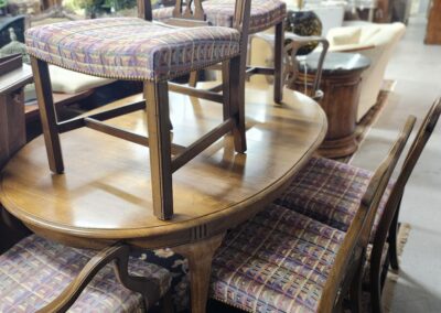 Wooden dining table with matching chairs stacked inside a store.