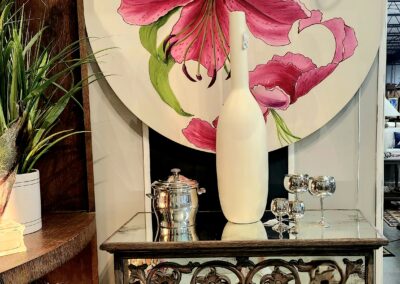 Elegant vase with pink flowers on ornate table beneath floral wall art.
