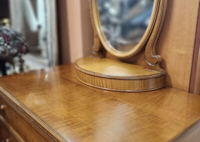 Close-up of a wooden dresser with an oval mirror in a cozy room.
