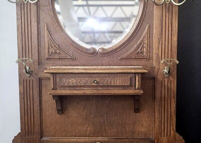 Antique wooden hall tree with ornate carvings, mirror, hooks, and a small shelf.