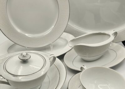 Elegant white porcelain dinnerware set with silver trim on gray surface.
