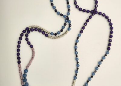 A long beaded necklace with blue and purple beads on a white surface.