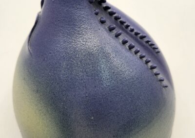 A blue and green ceramic vase with a unique stitched design.