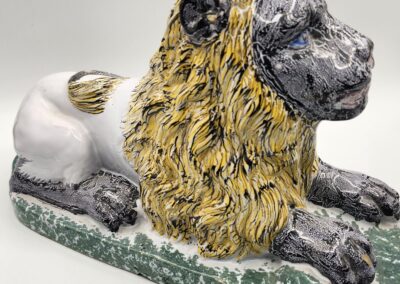Ceramic sculpture of a lion with a yellow mane and gray face.