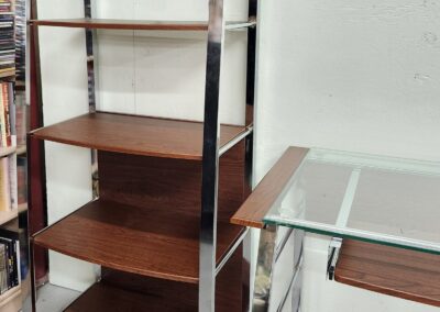 Modern shelving unit with wooden shelves and metal frame beside a glass desk.