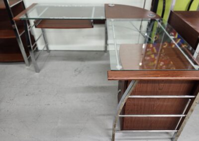 Glass-topped L-shaped office desk with wooden drawers and metal frame.