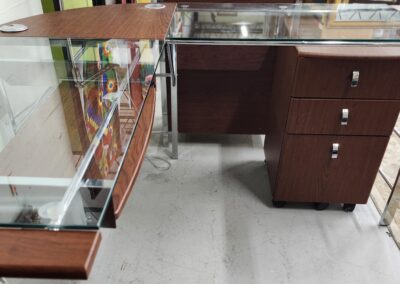 Modern glass-top desk with wooden drawers and metal frame.