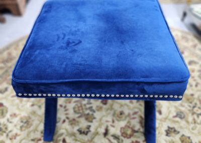 Blue velvet ottoman with studded trim on a patterned rug.
