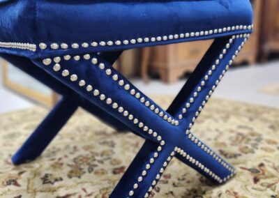 Blue leather stool with nailhead trim on a patterned rug.