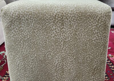 Beige textured ottoman on a patterned red rug.