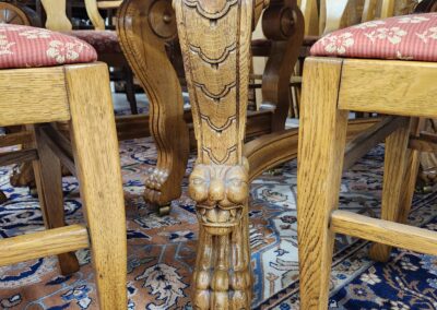 Ornately carved wooden table leg between two chairs on a patterned rug.