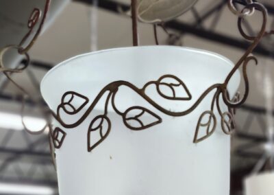 White hanging pot with decorative leaf patterns in a rustic setting.
