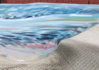 Close-up of a colorful, wavy glass bowl on a textured surface.