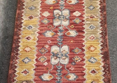 Colorful woven rug with geometric and floral patterns in red, yellow, and beige.