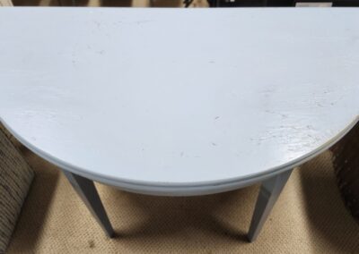 A small white semi-circular table with metal legs on a beige floor.