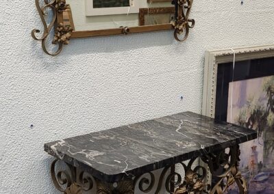 Elegant marble-topped console table with ornate wrought iron base beneath a decorative framed mirror.