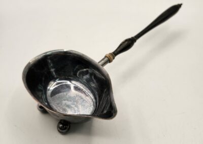 Antique silver ladle with ornate handle and three feet.