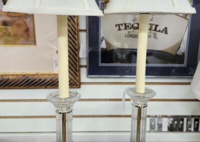 Pair of vintage brass candlestick lamps with white shades on a table.