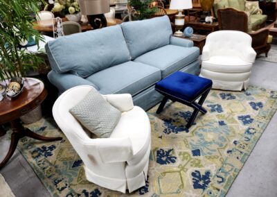 Cozy living room setup with blue sofa and white armchairs on a patterned rug.