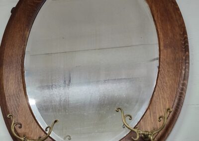Vintage oval mirror with wooden frame and brass hooks.
