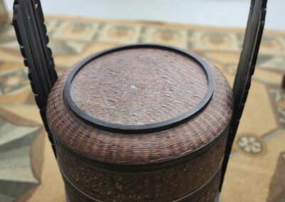 A vintage woven basket with a lid and handles, placed on a table.