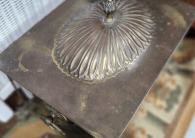 Antique metal box with ornate, shell-shaped lid on wooden table.