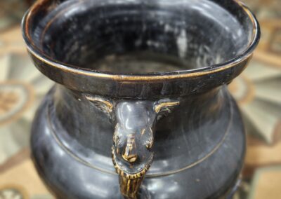 A black ceramic pot with a lion head decoration on its side.