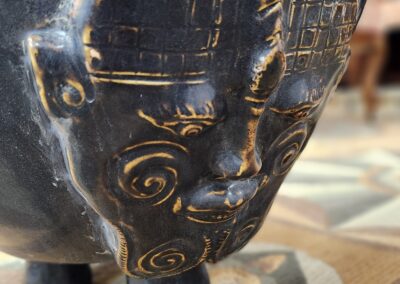 Close-up of a carved black wooden sculpture with intricate facial patterns.