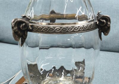 Clear glass vase with ornate metal handles on a table.