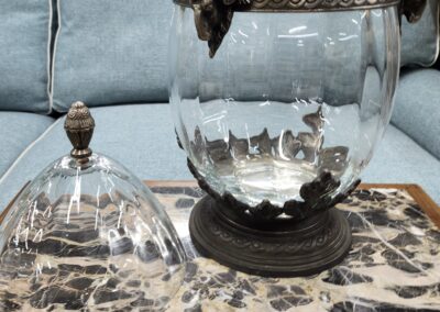 A vintage glass jar with a lid and ornate metal accents on a patterned cloth.