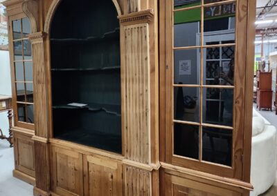Large wooden cabinet with glass doors and shelves in a showroom.