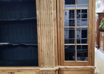 Large wooden bookcase with glass doors and shelves in a room.