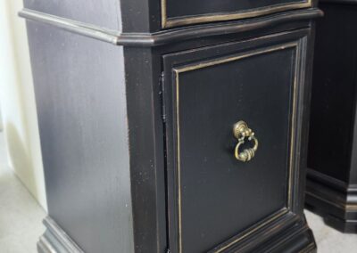 Elegant black wooden cabinet with gold accents and a drawer.