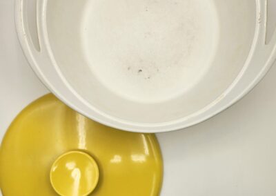 A cracked egg with yolk spilled near a white bowl on a light surface.