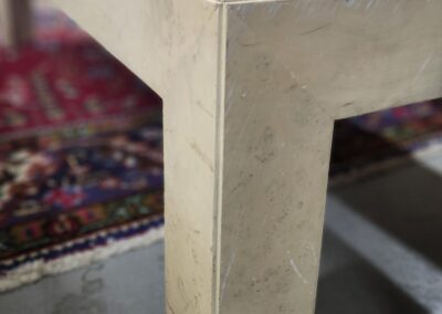 Close-up of a beige marble table leg with a decorative rug in the background.