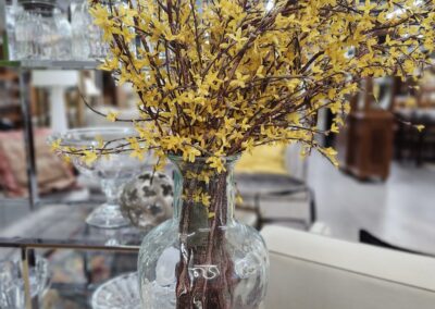 A glass vase with yellow flowers on a white table in a store.