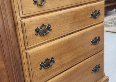 Wooden chest of drawers with ornate handles in a warm finish.