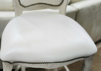 White cushioned chair with nailhead trim and carved legs.